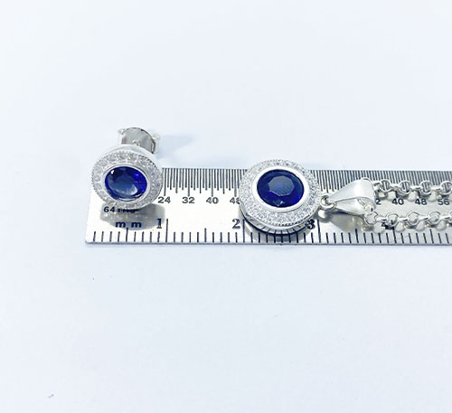 Set de aretes, dije, y cadena de plata ley 0,925 con zafiro creado, talla redonda de tamaño 5,5 mm de diámetro en el dije y en los aretes . El zafiro creado en laboratorio tiene la misma composición química y  un alto parecido en su aspecto, color y brillo al zafiro natural. Acompañado de chispas de circón de 1,0 mm C/U. -Incluye cadena de plata de 45 cm y 3 gramos de peso.